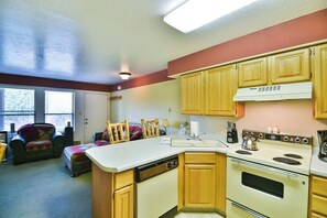 A compact kitchen with wooden cabinets, a built-in dishwasher, a stove, and a window providing natural light.