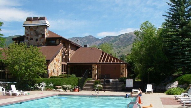 Ein Schwimmbad mit Liegestühlen, ein Steinhaus mit einem Turm und Berge im Hintergrund.