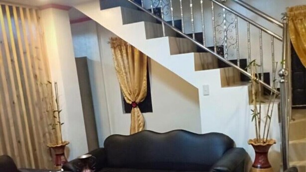 A living room with a black leather sofa, a glass coffee table, and a staircase with a metal railing.