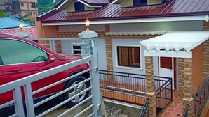 A residential building with a stone facade, a red car parked in front, and a gated entrance.