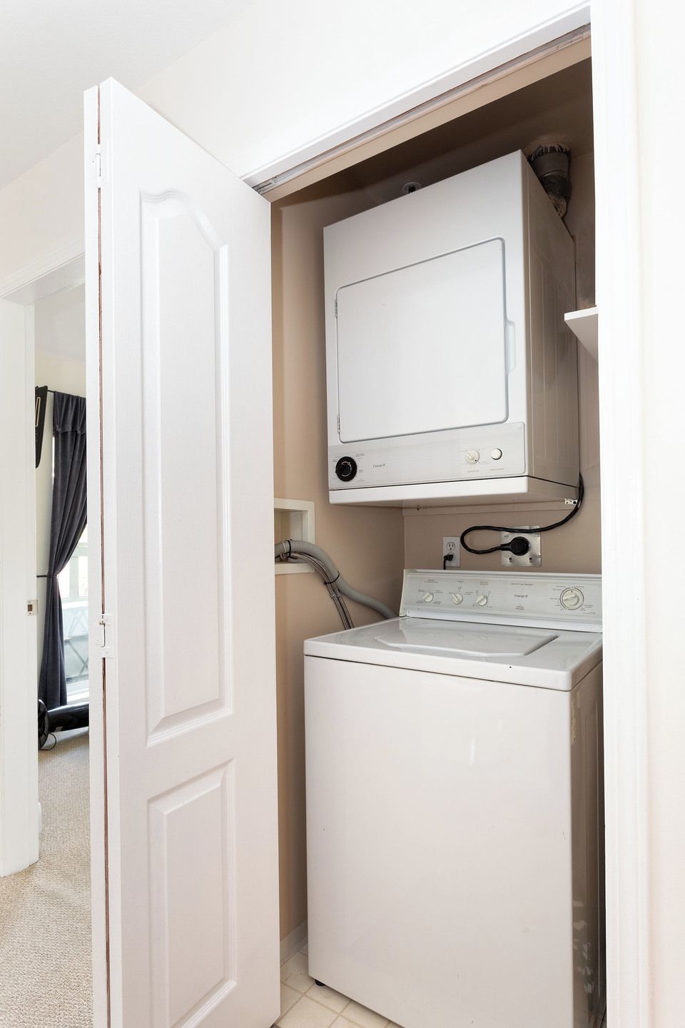 Une petite buanderie équipée d’un lave-linge et d’un sèche-linge à chargement frontal, d’un petit meuble de rangement au-dessus du sèche-linge et d’une prise électrique visible.