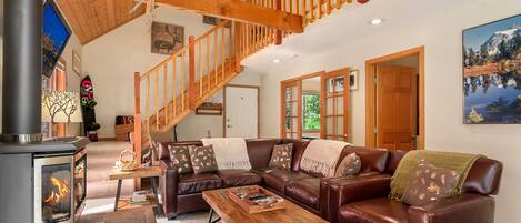 A cozy living room with a fireplace, leather sofa, wooden coffee table, and a staircase.