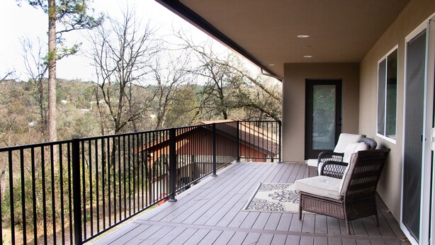 A wooden deck with a black railing, a wicker chair, and a door leading to a screened area. -  Country Setting in the Heart of Gold Country - Yet close to it all (Placerville)