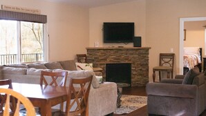 A living room with a stone fireplace, a television mounted above it, and a dining area with wooden furniture. -  Country Setting in the Heart of Gold Country - Yet close to it all (Placerville)