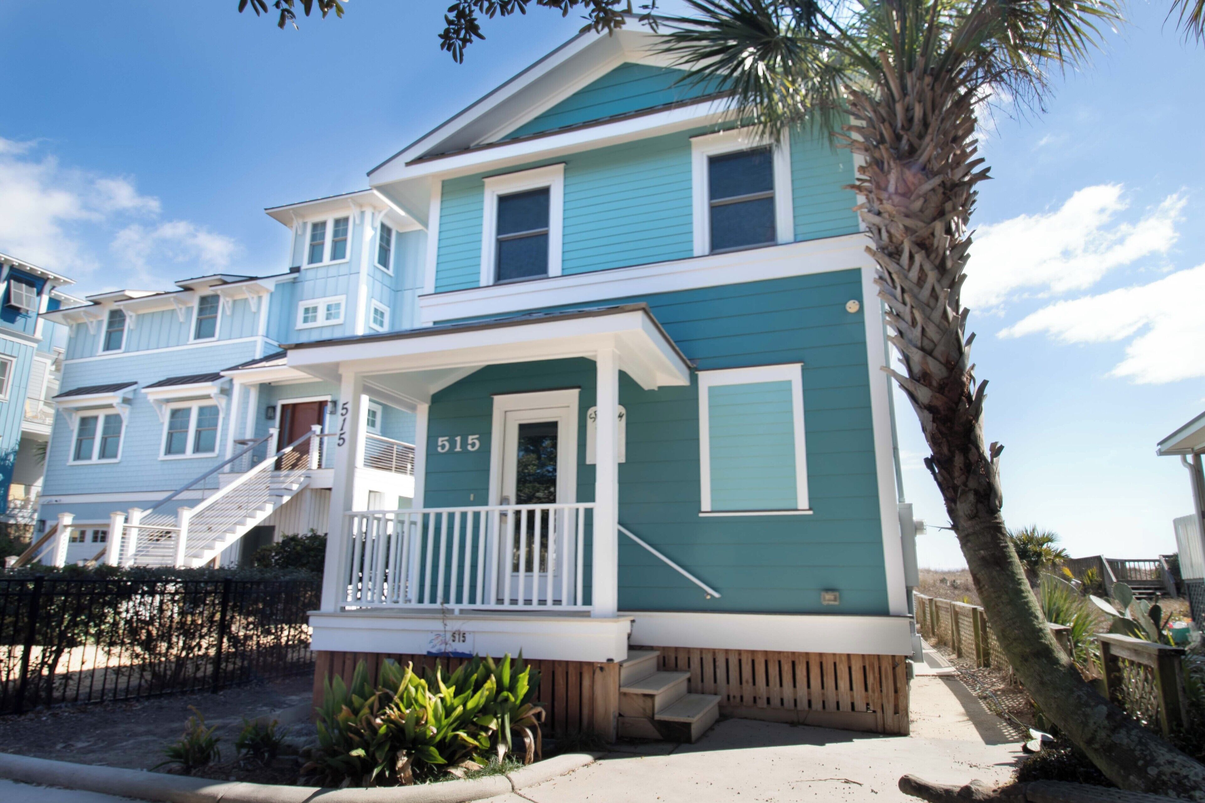 A two-story house with a blue exterior and white trim, featuring a front porch with steps and a small garden area.