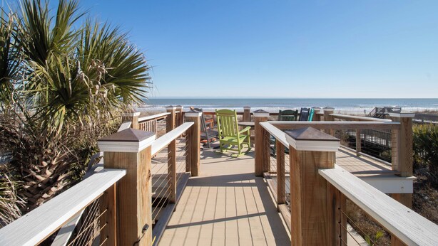 Eine Holzterrasse führt zu einem Strand mit einem Stuhl und einem Tisch mit Blick auf den Ozean.