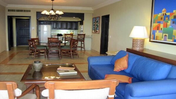 A living room with a blue sofa, wooden chairs, a coffee table, and a dining area with a chandelier.