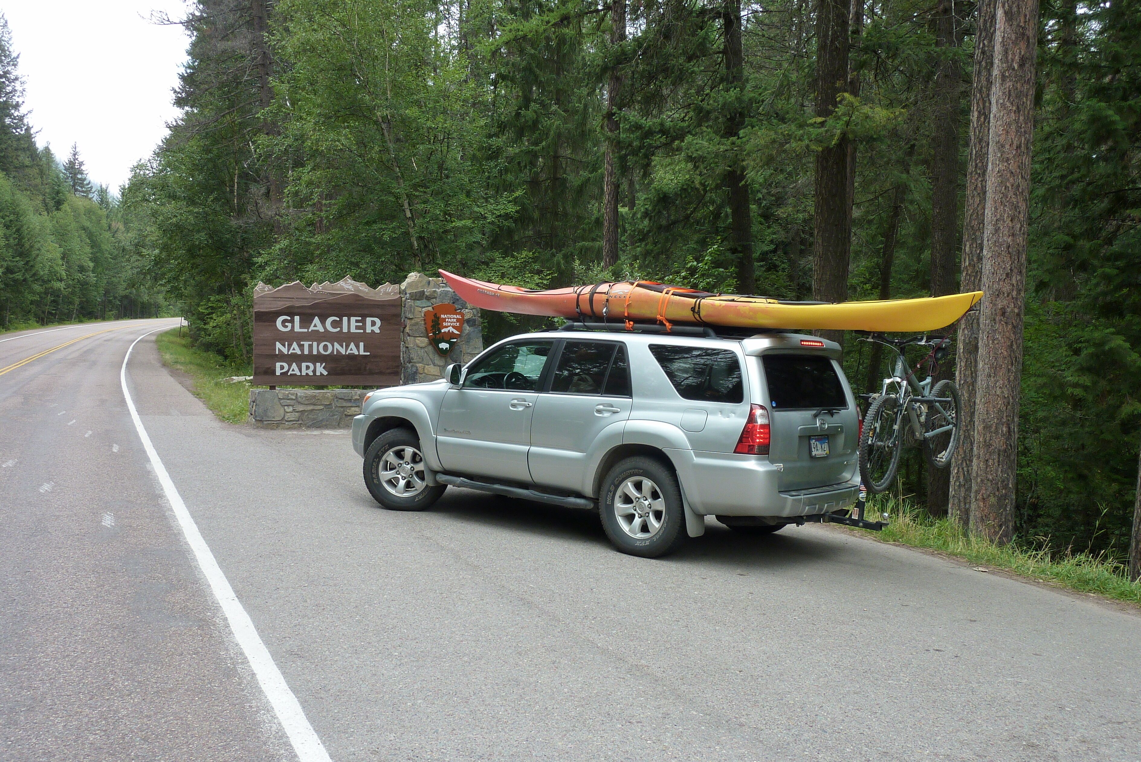 En bil parkeret i nærheden af et skilt for Glacier National Park.