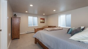Un dormitorio con cama, mesita de noche, armario de madera y dos ventanas con persianas.