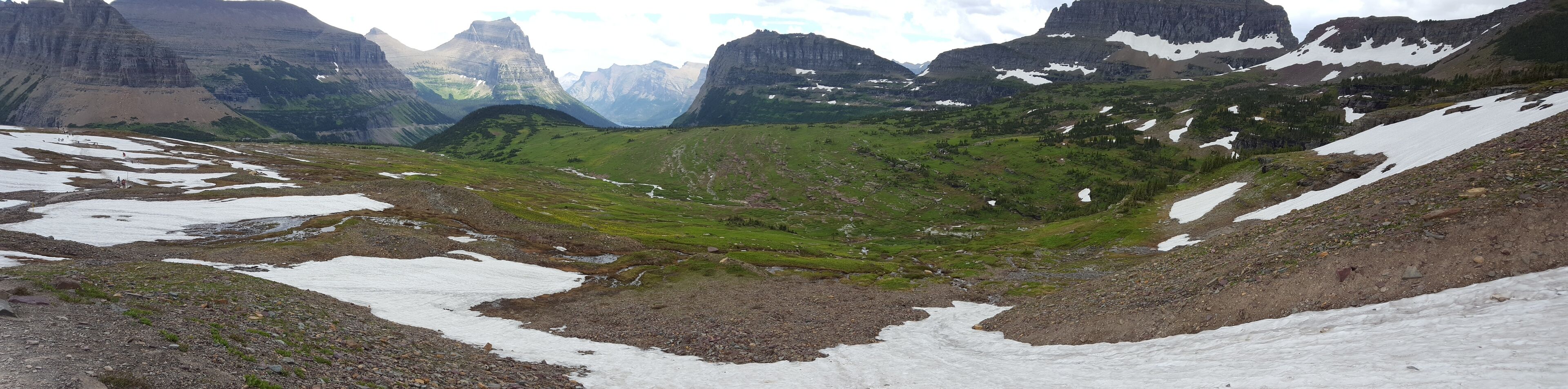 Un paysage montagneux parsemé de zones enneigées et de vallées verdoyantes.