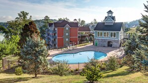 Zona residencial con piscina rodeada por una cerca, un pequeño edificio con torrecilla y un edificio grande de varios pisos con balcones.