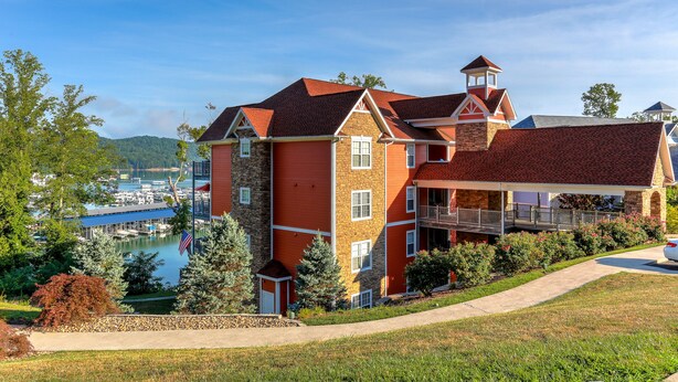 Un hotel de varios pisos con fachada de piedra, techo rojo y vistas a un puerto deportivo.