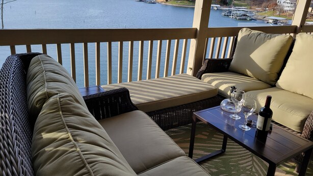 Ein Balkon mit einer Couch und einem Tisch, mit Blick auf ein Gewässer und eine Brücke.