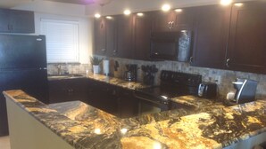 Una cocina con armarios de madera oscura, encimera de granito, refrigerador negro y microondas empotrado.