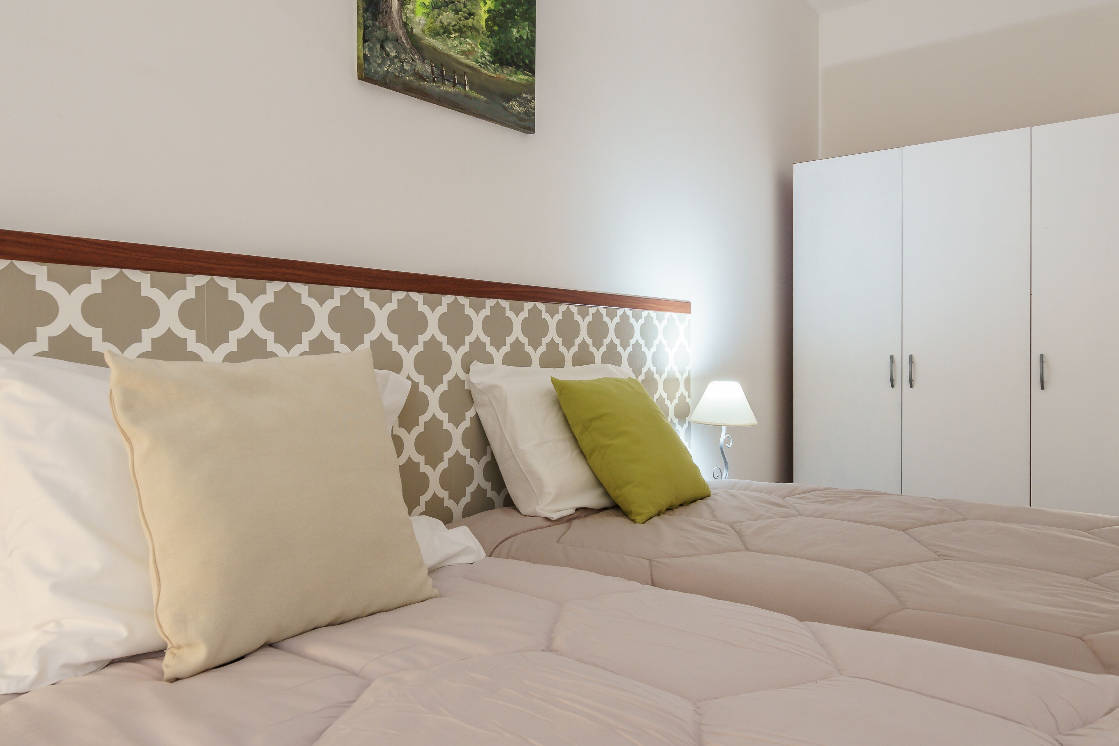 A neatly made bed with a patterned headboard, a bedside lamp, and a wardrobe.
