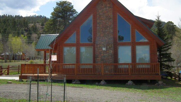 Una cabaña con fachada de piedra, amplias ventanas y una terraza de madera.