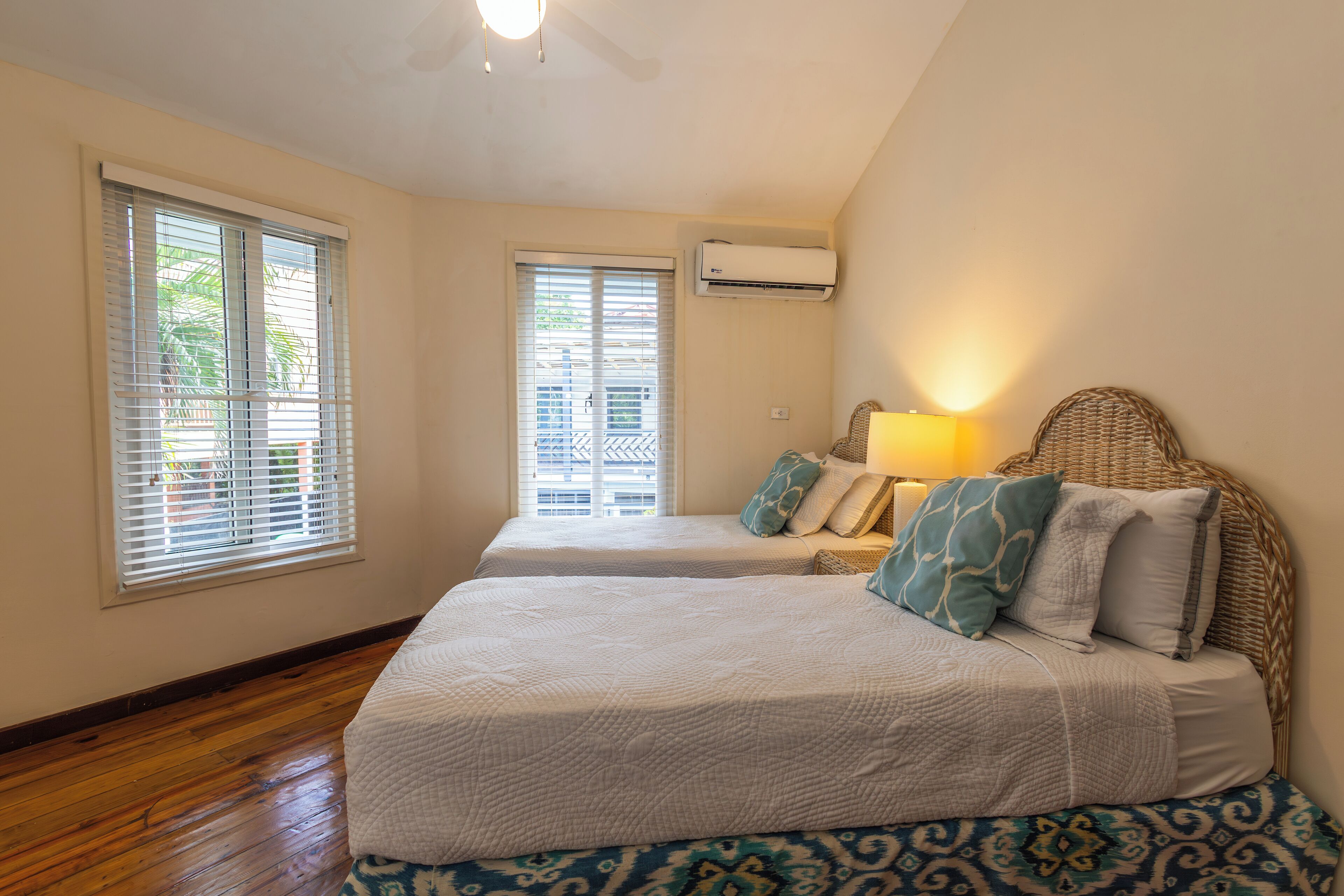 A bedroom with two beds, a ceiling fan, an air conditioning unit, and a window with blinds.