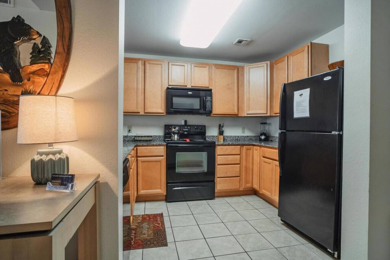 A compact kitchen with wooden cabinets, a black refrigerator, a microwave, and an oven.