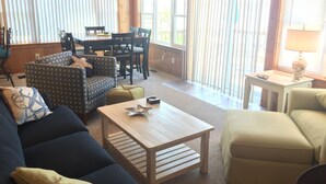 A cozy living room with a sofa, armchair, and a coffee table. There is a dining table with chairs and a window with blinds. - Waterfront Cottage w Private Beach on Chesapeake Bay! (Grimstead)