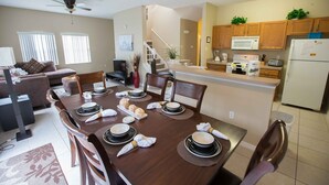 A dining area with a wooden table set for four, surrounded by chairs. A kitchen is visible in the background with wooden cabinets and a microwave. - Special rates available in Sep and  Oct of 2026 (Kissimmee)