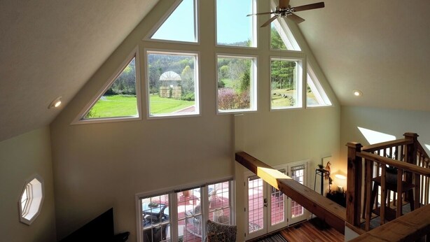 A spacious room with large windows, a wooden staircase, and a ceiling fan. - Come and enjoy a beautiful view and relaxing time at Windy Knoll.... (Afton)