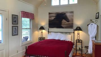 A bedroom with a bed, two bedside lamps, a large abstract painting, a window with curtains, and a ceiling fan.