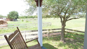 A wooden bench under a white gazebo with a view of a fenced pasture and a tree.