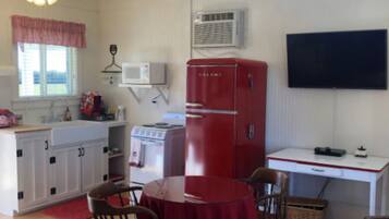 A compact kitchen with a red refrigerator, a microwave, and a stove. There is a dining table with chairs and a ceiling fan above.