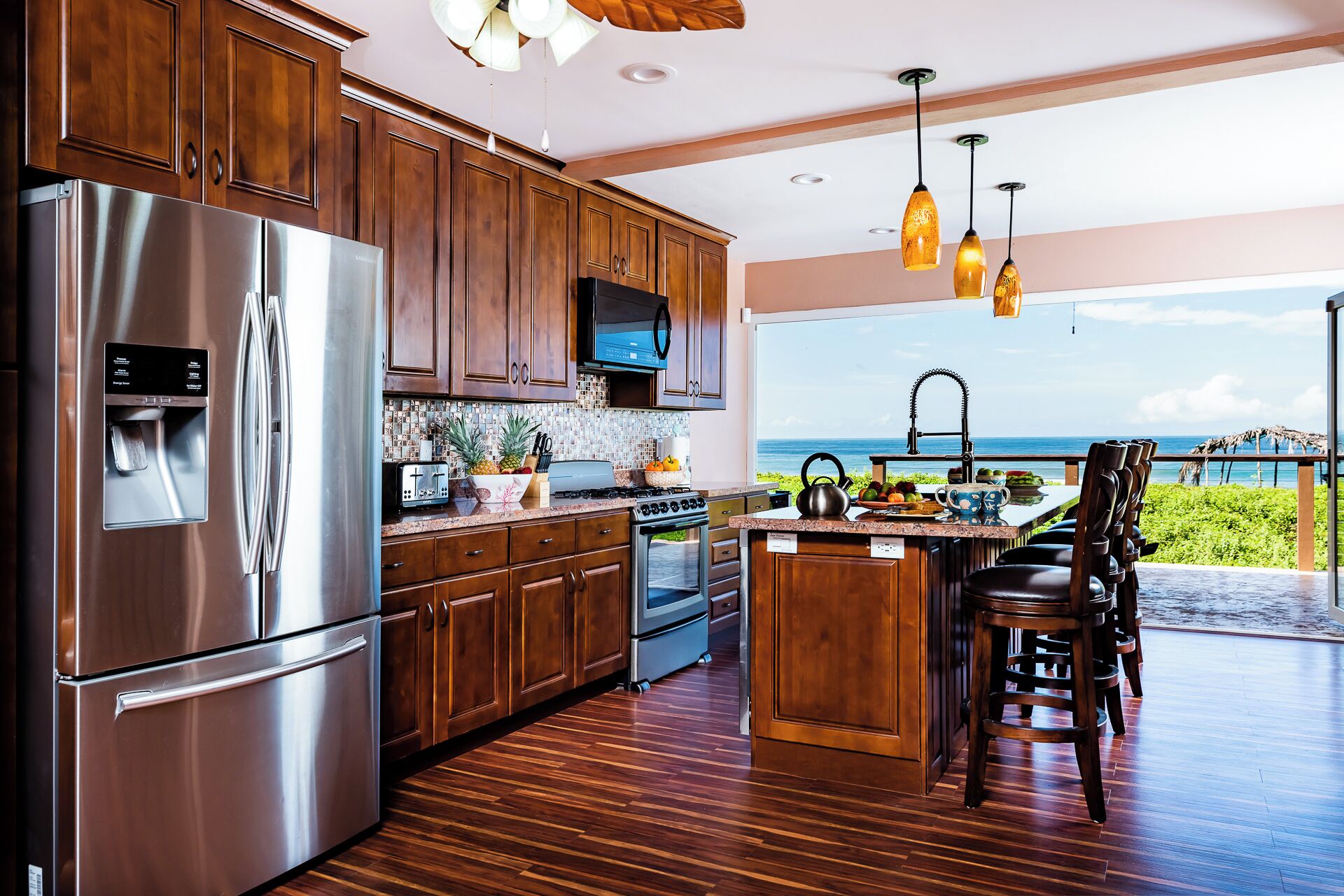 A modern kitchen with stainless steel appliances, wooden cabinets, and a view of the ocean.