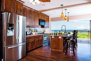 Cocina moderna con electrodomésticos de acero inoxidable, armarios de madera y vista al océano.