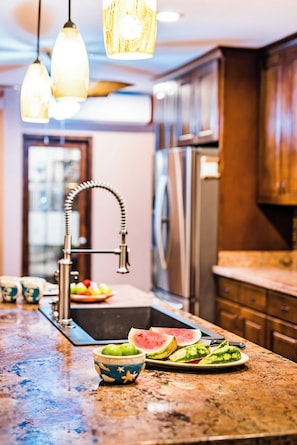 Una cocina con encimera de granito, electrodomésticos de acero inoxidable y una lámpara colgante.