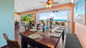 Un coin repas avec vue sur l’océan, un ventilateur de plafond et une table dressée pour six personnes.