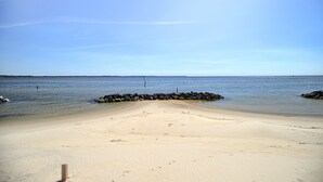 A sandy beach with calm water, a wooden post, and a rocky breakwater.