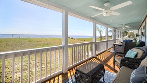 A covered porch with wicker furniture, a view of the beach, and a ceiling fan.