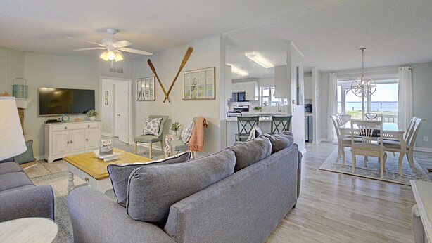 A spacious living area with a grey sofa, a television, and a dining area with a table and chairs.