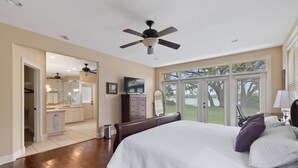 Un dormitorio con una cama grande, un ventilador de techo, un televisor y vistas al exterior.