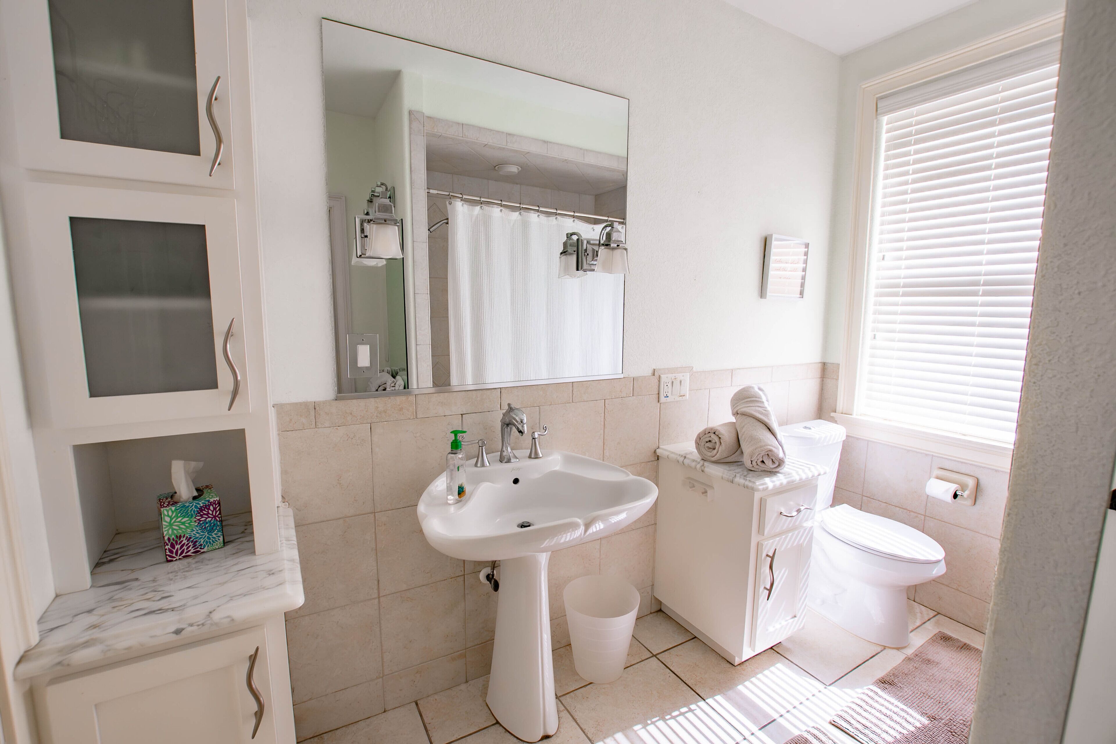 Une salle de bain avec un lavabo, des toilettes et un miroir. On y trouve également un porte-serviettes et une poubelle.