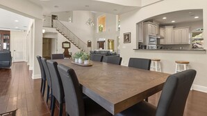 Un comedor amplio con una gran mesa de madera, sillas negras y una escalera que sube a un nivel superior.