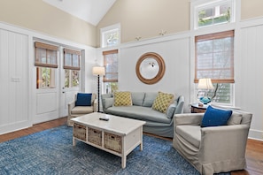A living room with a sofa, armchairs, a coffee table, and a round mirror.