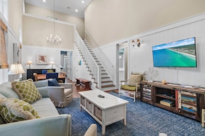 A spacious living room with a large flat-screen TV, a staircase, and a cozy seating area.