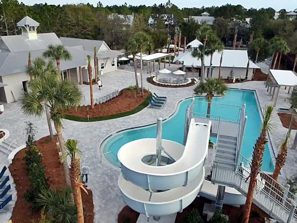A pool area with a water slide, palm trees, and a covered seating area.