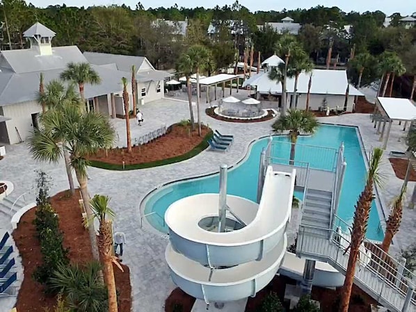 A pool area with a water slide, palm trees, and a covered seating area.