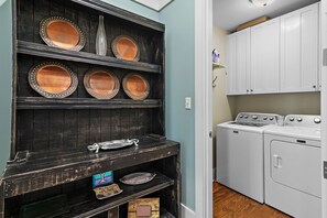 A laundry room with a washing machine and dryer, a shelf with decorative plates, and a wall-mounted light fixture. - 35 Lyonia-Watercolor-Community Pool-3 bikes (Santa Rosa Beach)