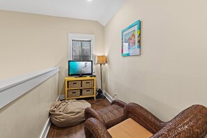 Sala de estar com televisão, luminária, sofá de vime e janela.