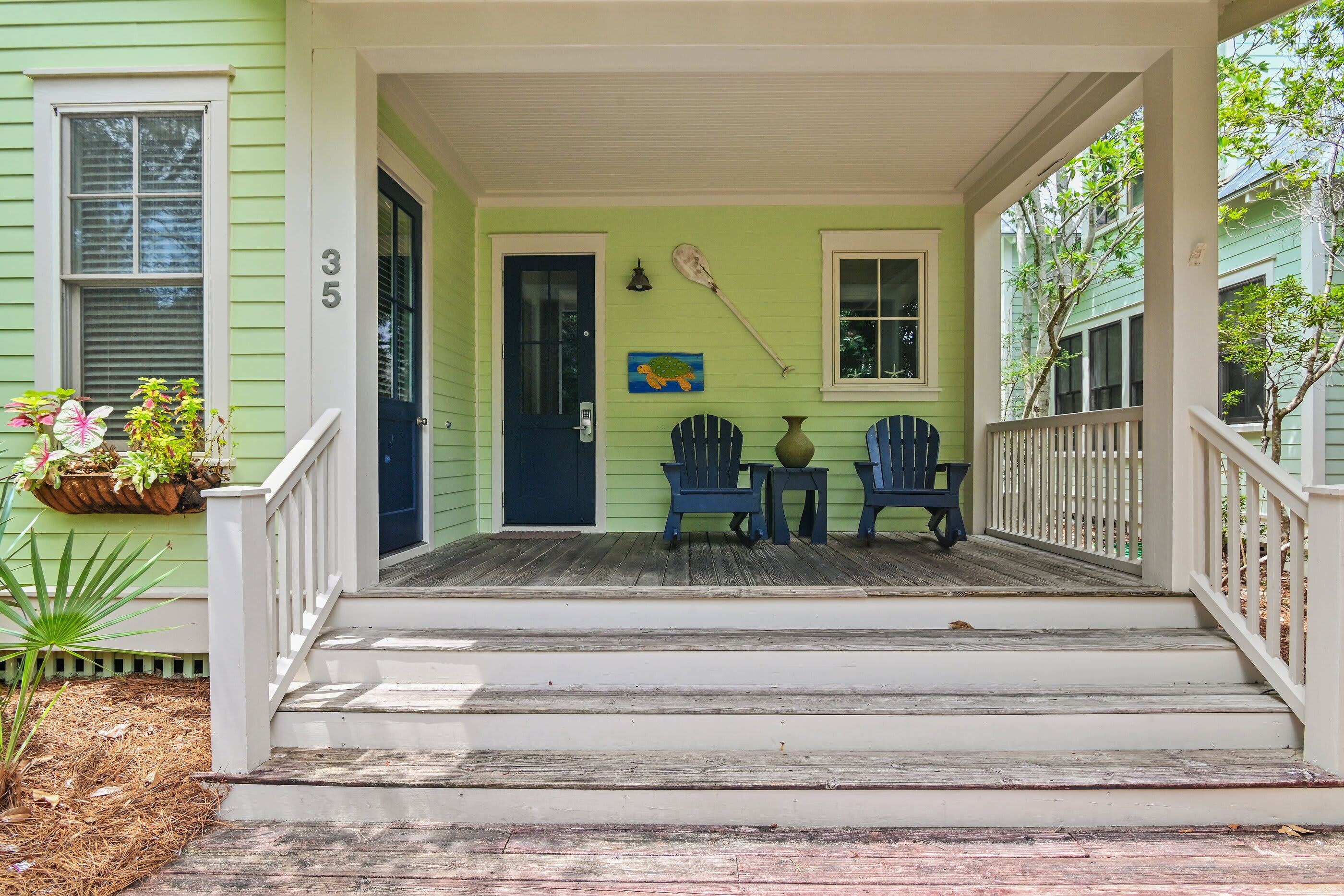 A porch with a dark door, two blue chairs, a small table, and a potted plant.