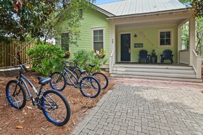 A green house with a porch, two bicycles parked outside, and a brick pathway leading to the entrance. - 35 Lyonia-Watercolor-Community Pool-3 bikes (Santa Rosa Beach)