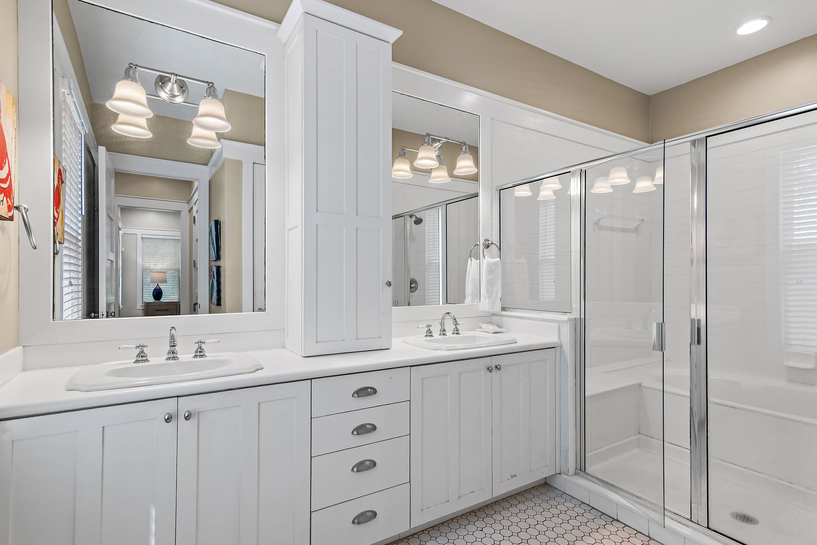 A modern bathroom with a double sink vanity, a large mirror, and a glass-enclosed shower.