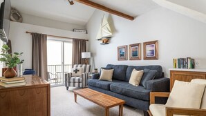 A cozy living room with a sofa, armchair, wooden coffee table, and a bookshelf.
