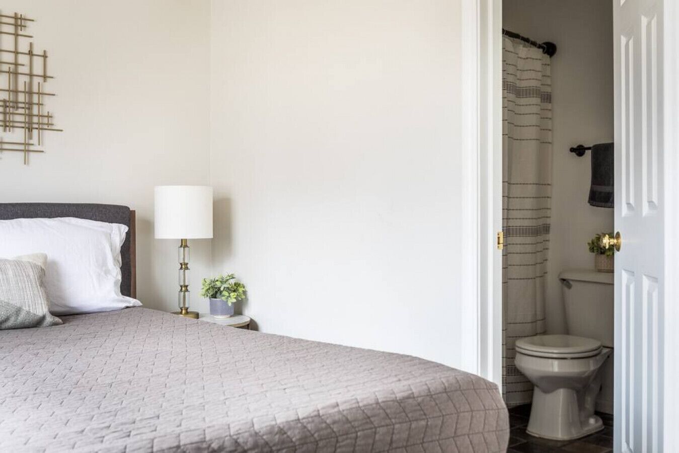 A bedroom with a bed, bedside lamp, and a small potted plant.