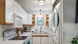 A compact kitchen with white cabinets, a stove, a sink, and a dishwasher.